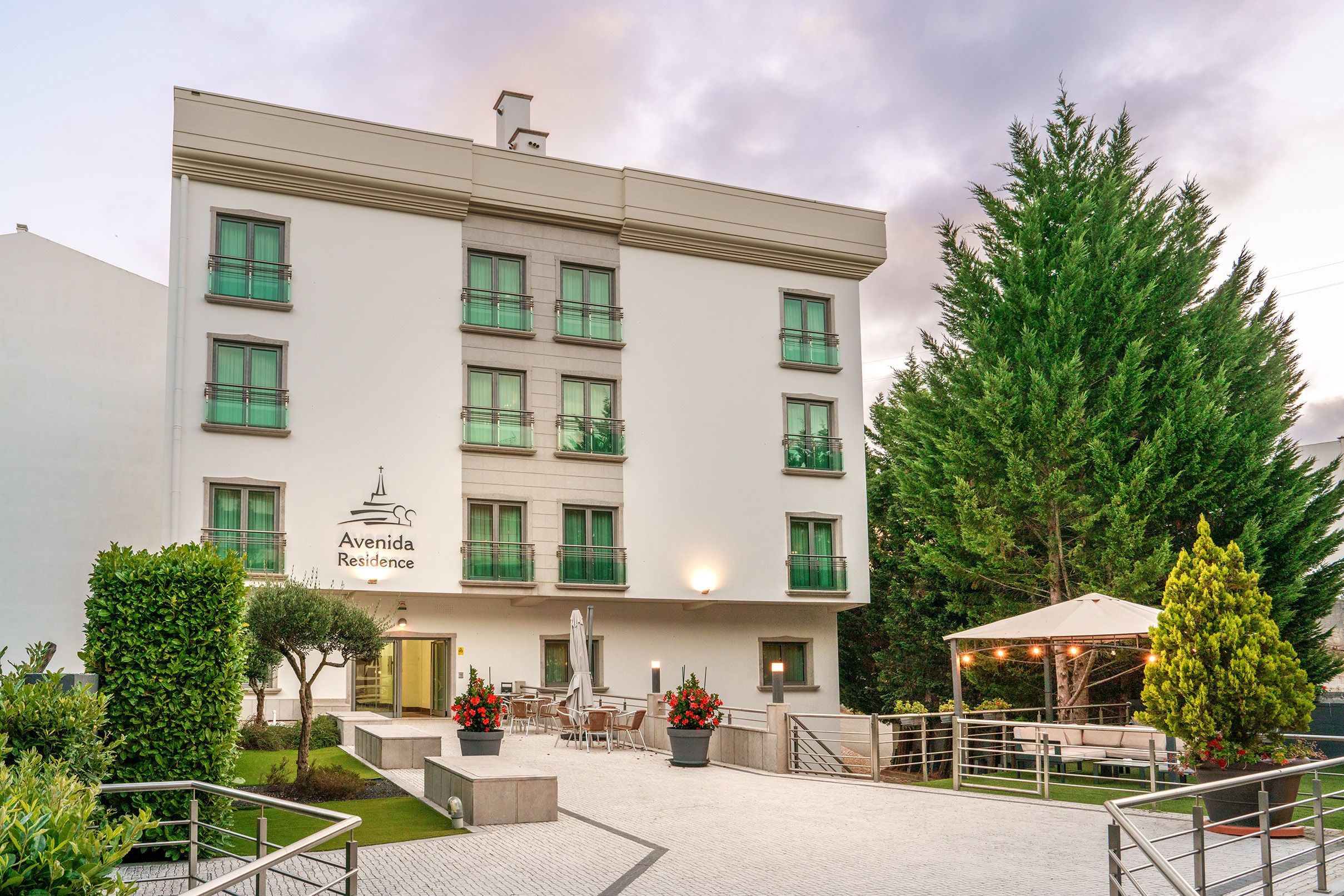 A multi-story hotel with a flat facade, outdoor seating area, and a gated entrance.