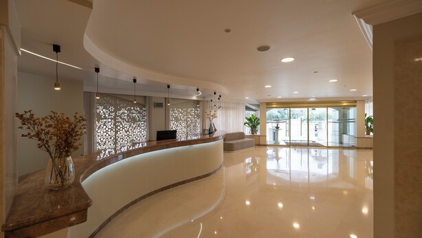 A modern hotel lobby with a curved reception desk, a seating area, and a large glass door entrance.