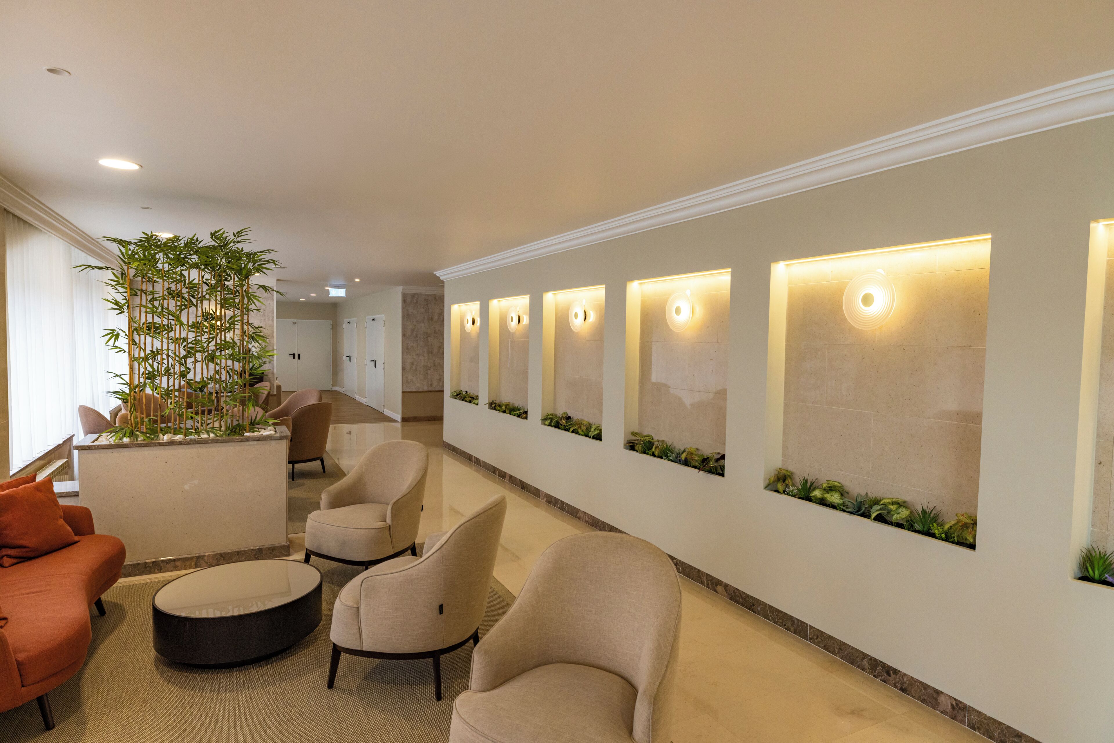 A modern lobby with seating, a large plant, and wall-mounted lighting.