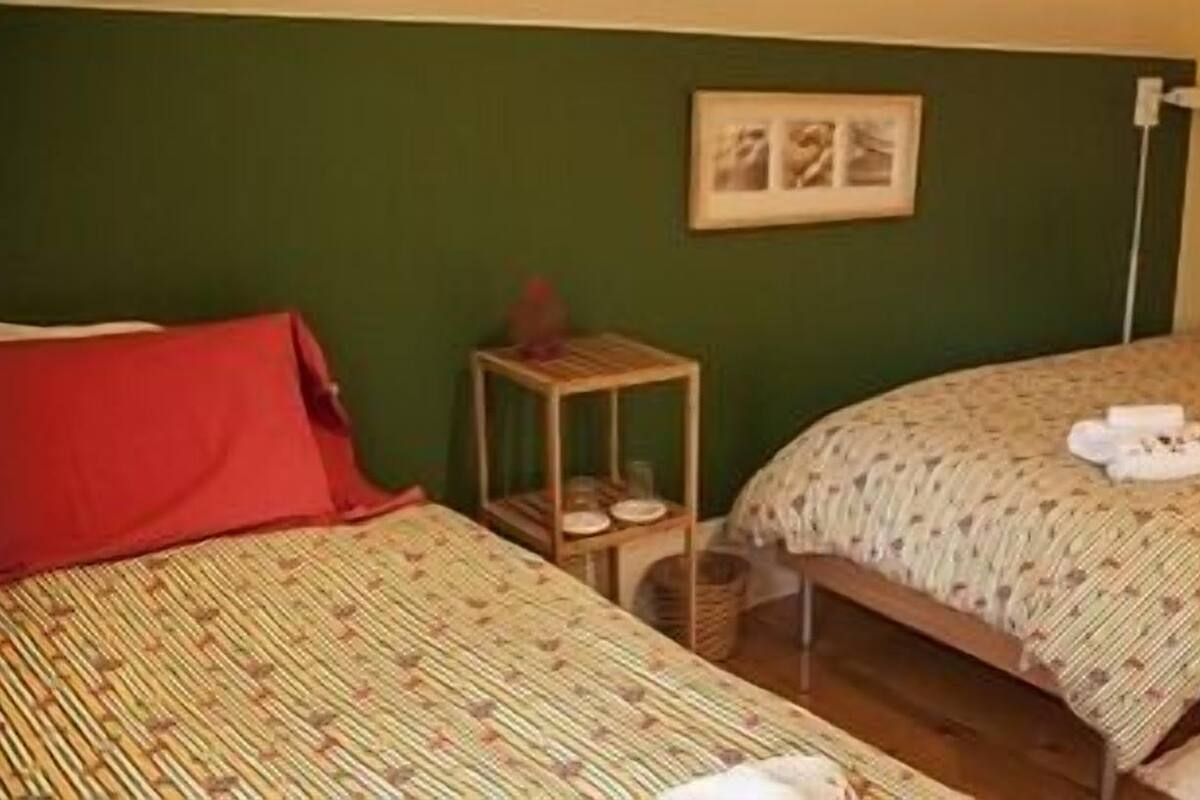A room with two beds, a small table, a framed picture on the wall, and a door with a towel hanging on it.