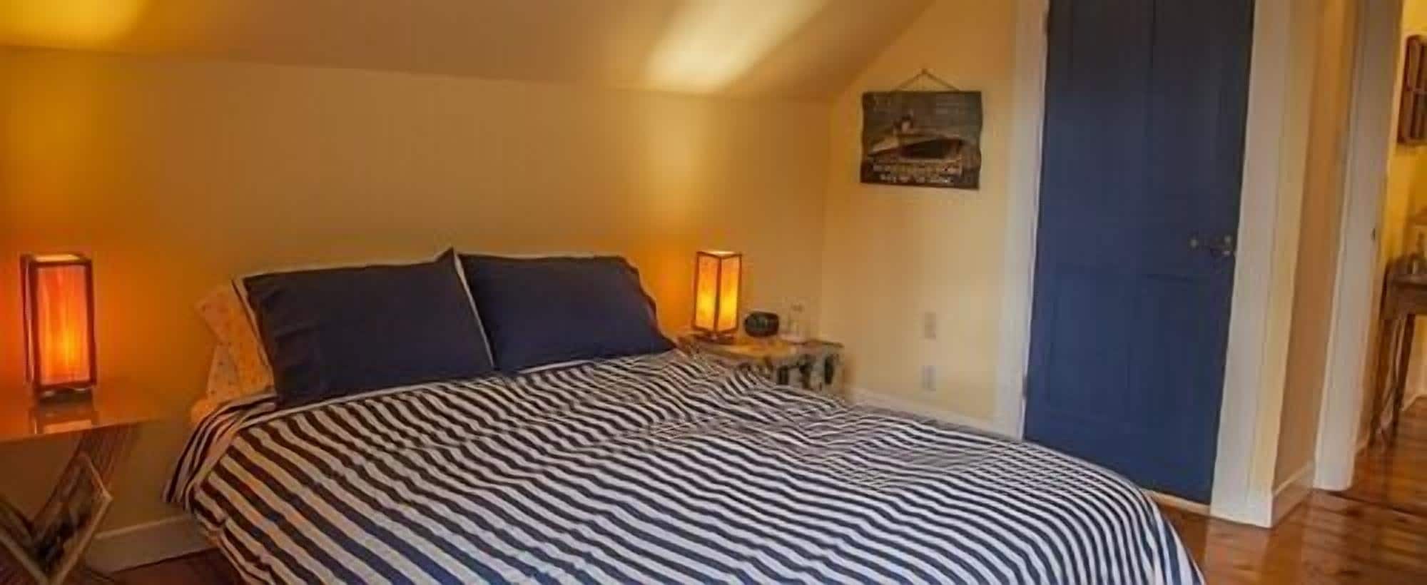 Un dormitorio con una colcha a rayas, dos lámparas de noche y una puerta.