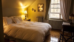 Un dormitorio acogedor con una cama grande, una mesita de noche con lámpara, un radiador y una ventana con cortinas.