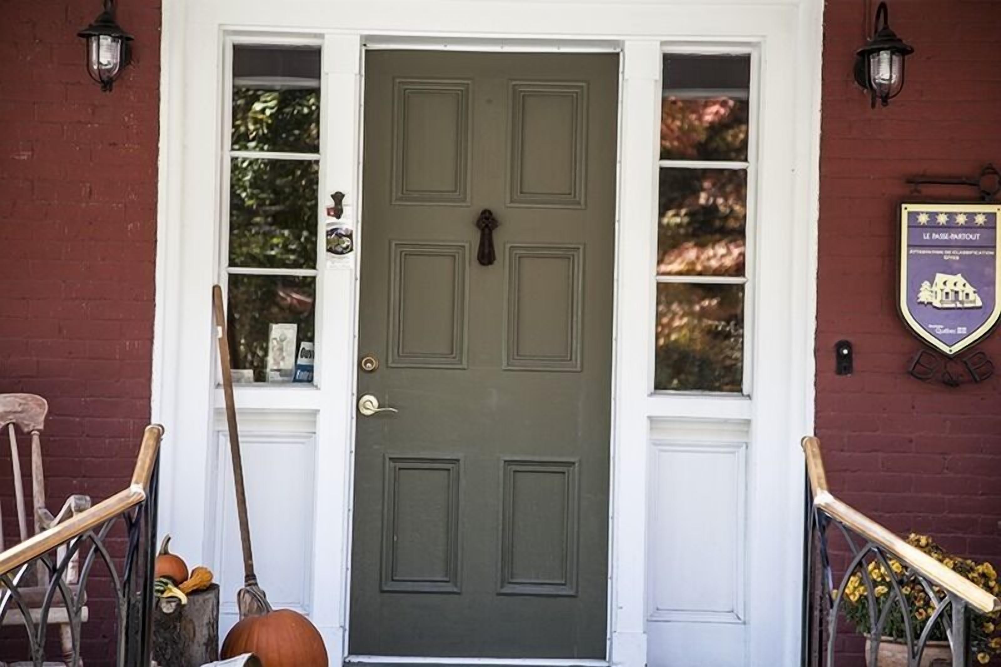 A green door with a brass knocker, flanked by windows with white frames and a brick wall.