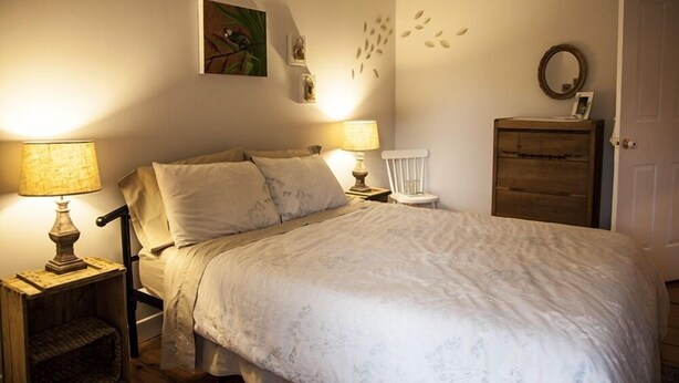 Une chambre à coucher comprenant un lit, deux lampes de chevet, une chaise, une commode et des éléments décoratifs sur les murs.