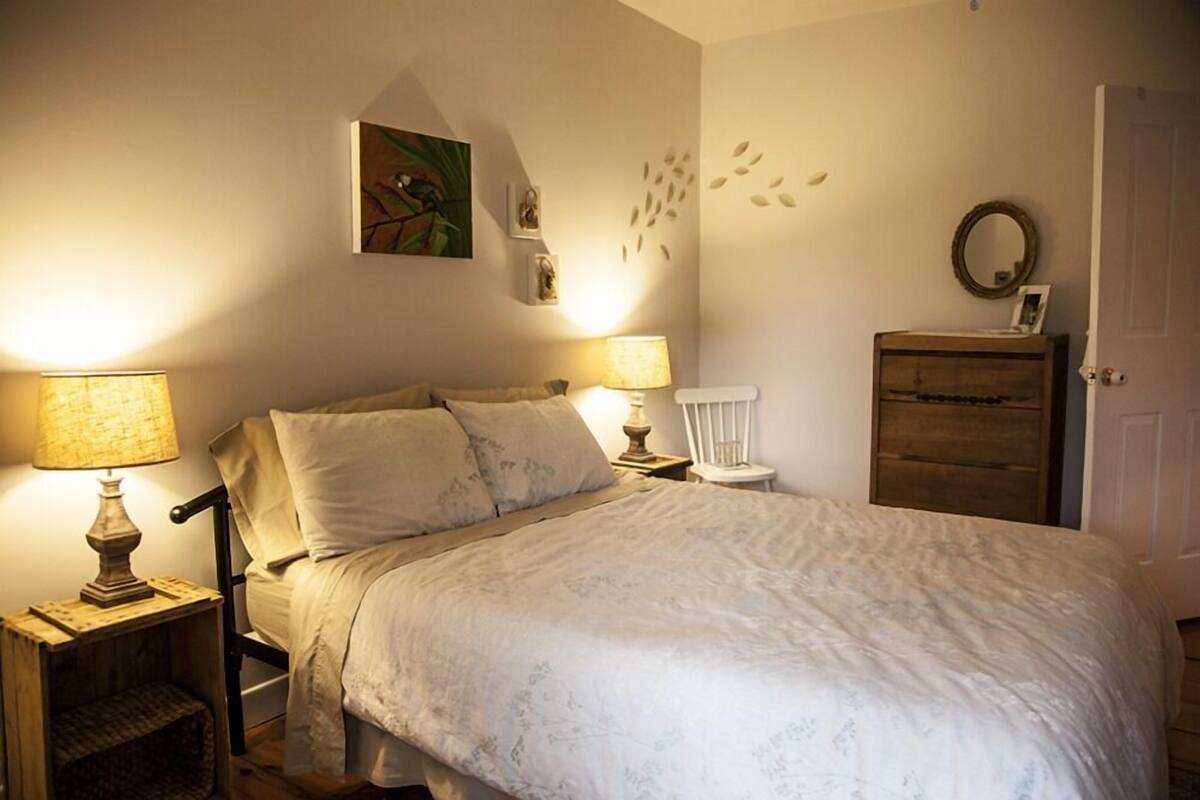 A bedroom with a bed, two bedside lamps, a chair, a dresser, and wall decorations.