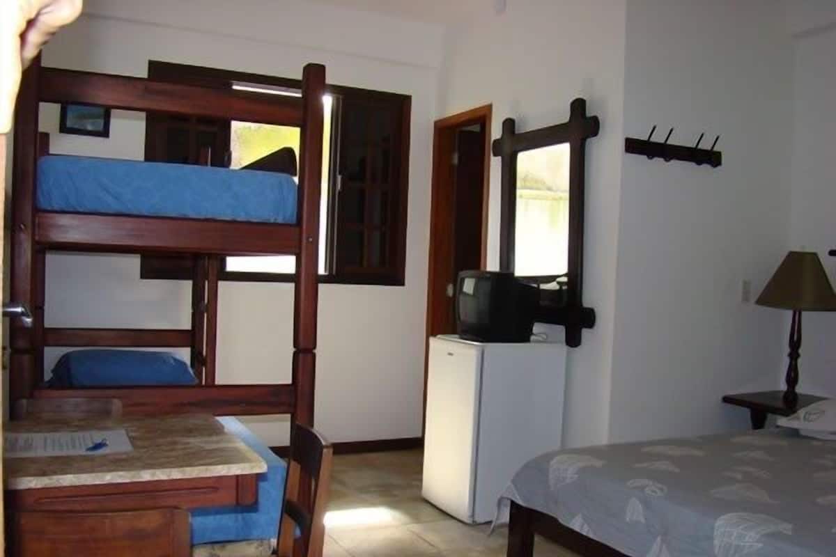 Ein kleines Zimmer mit Etagenbett, einer kleinen Küchenzeile, einem Tisch mit Stühlen, einer Lampe und einem Spiegel an der Wand.