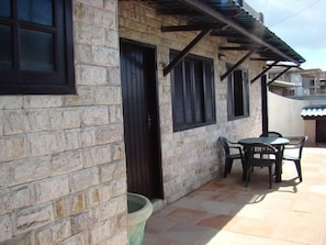 A stone building with a black door and windows, a patio with a table and chairs, and a tiled floor. - Pousada Casa do Telhado Verde (Cabo Frio)