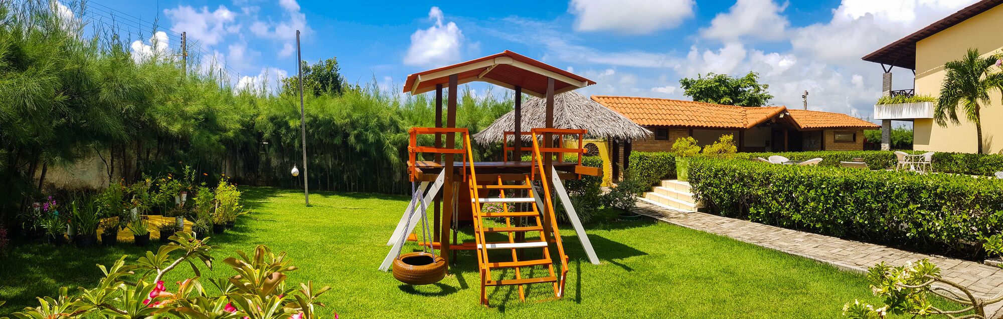 A playground with a slide and a climbing structure, surrounded by well-maintained grass and plants.