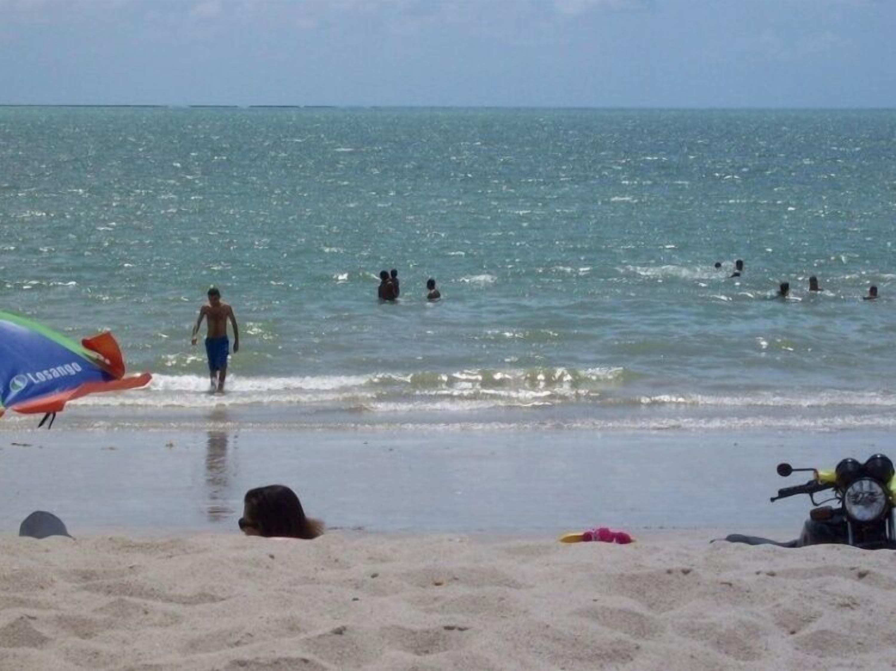A beach with people swimming and a surfboard in the sand.