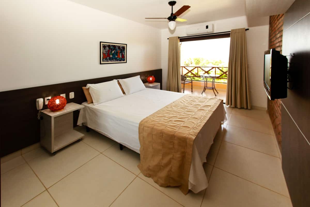 A hotel room with a bed, a nightstand, a TV, and a balcony with a table and chairs.