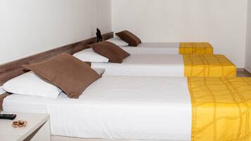 Habitación de hotel con tres camas individuales, cada una con un edredón de diferente color. Hay una mesita con un control remoto y un aperitivo encima.