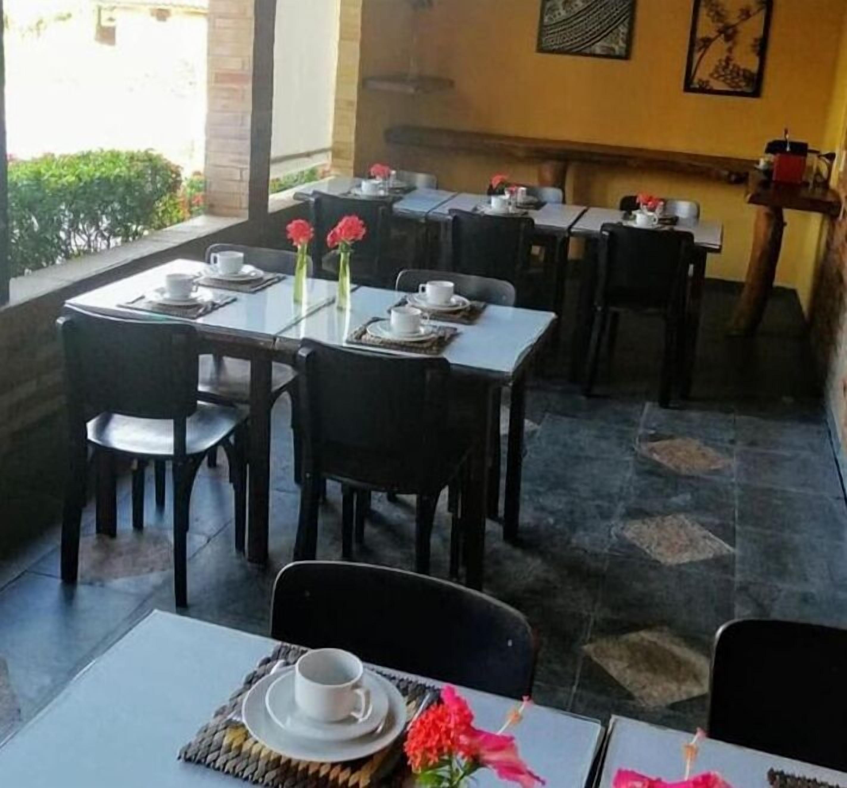 Un restaurant amb terrassa, taules preparades amb tasses i platets blancs, i flors vermelles sobre les taules.