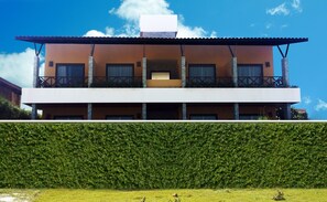 Un edificio moderno di due piani con tetto piatto, balconi e un cespuglio ben curato di fronte.