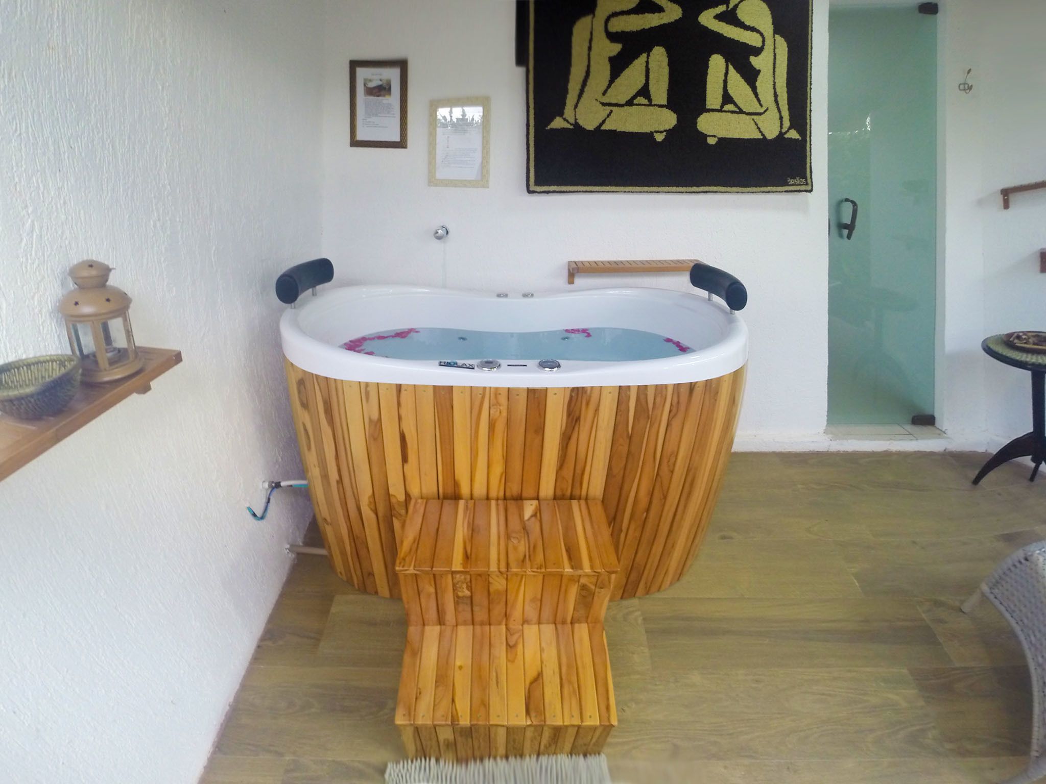 A wooden bathtub in a room with a wooden floor, a small table, and a green door.