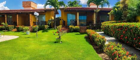 A two-story building with a pool, surrounded by well-maintained gardens and a clear sky.