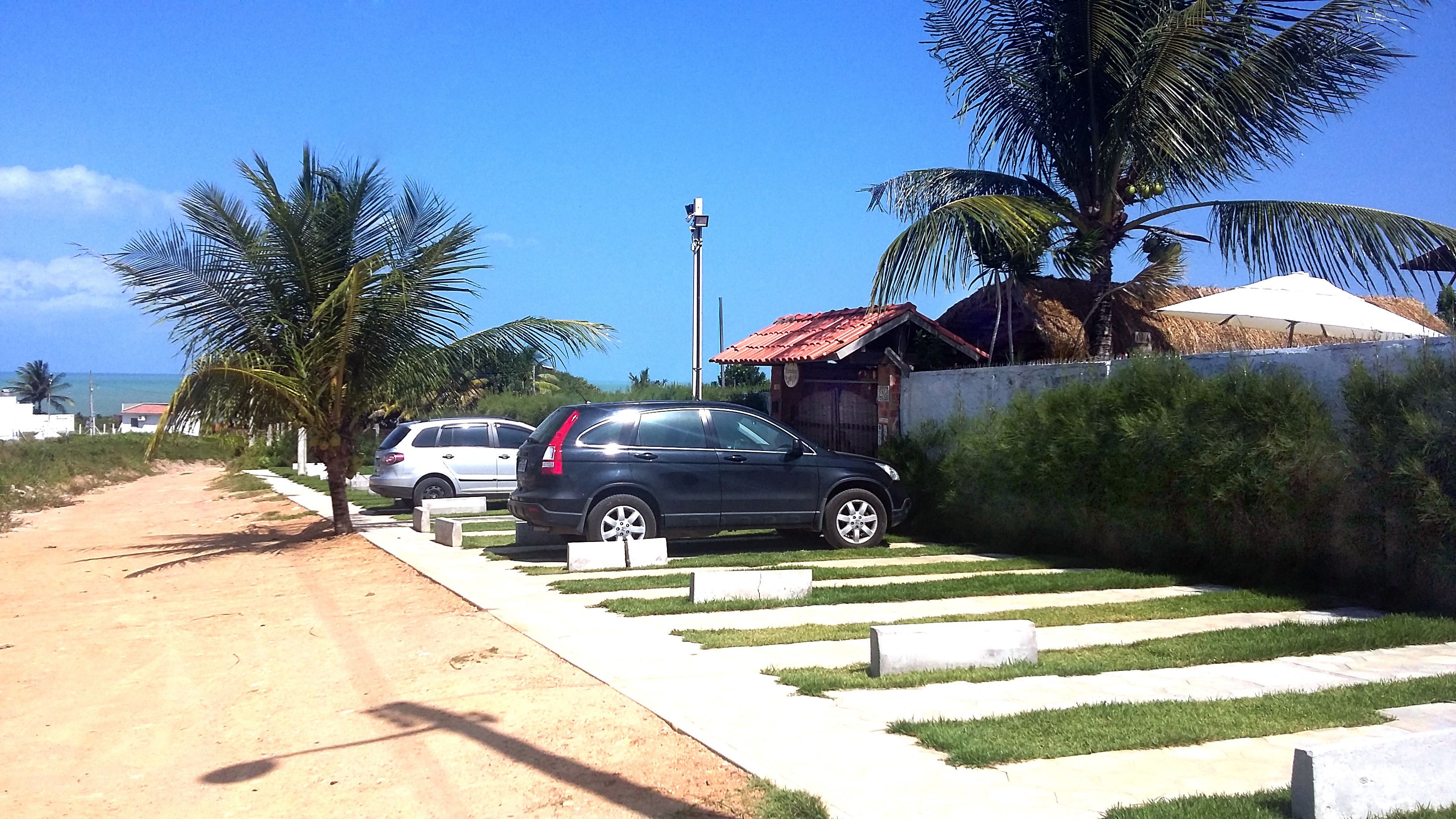 A parking area with two cars, a dirt path, and a white building with a red roof.