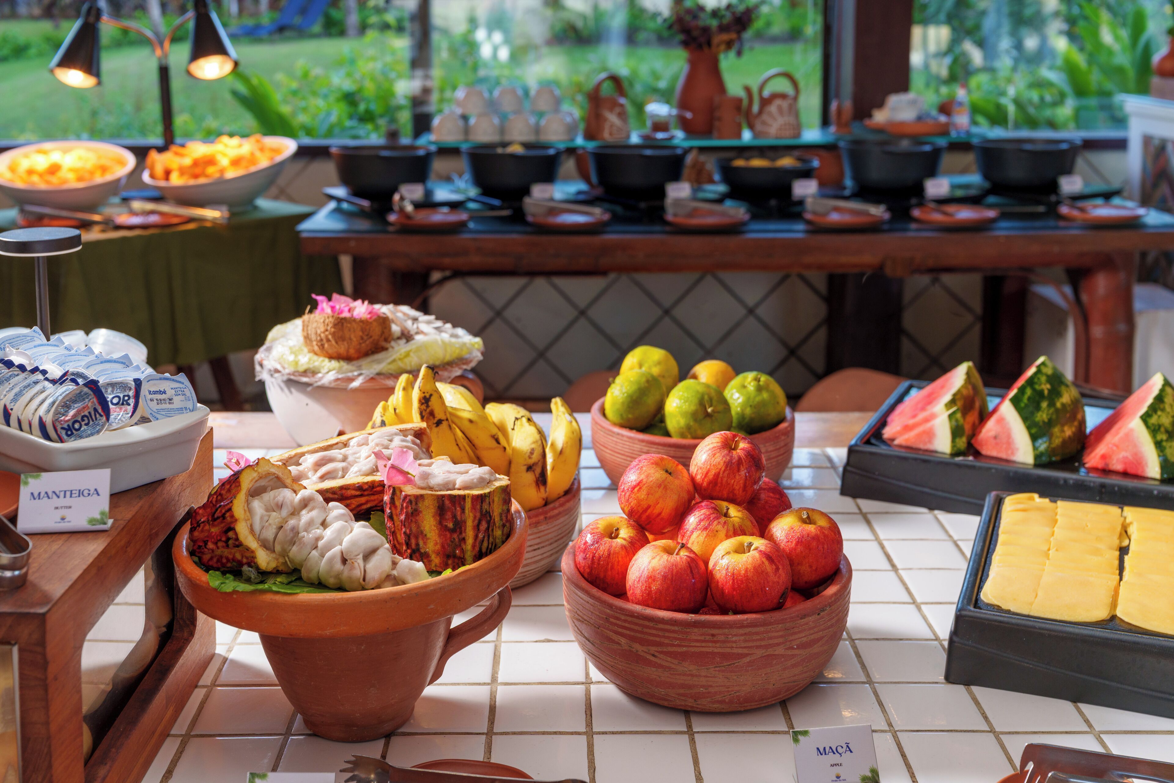 A buffet table with various food items including fruits, a bowl of apples, and a dish with a decorative centerpiece.