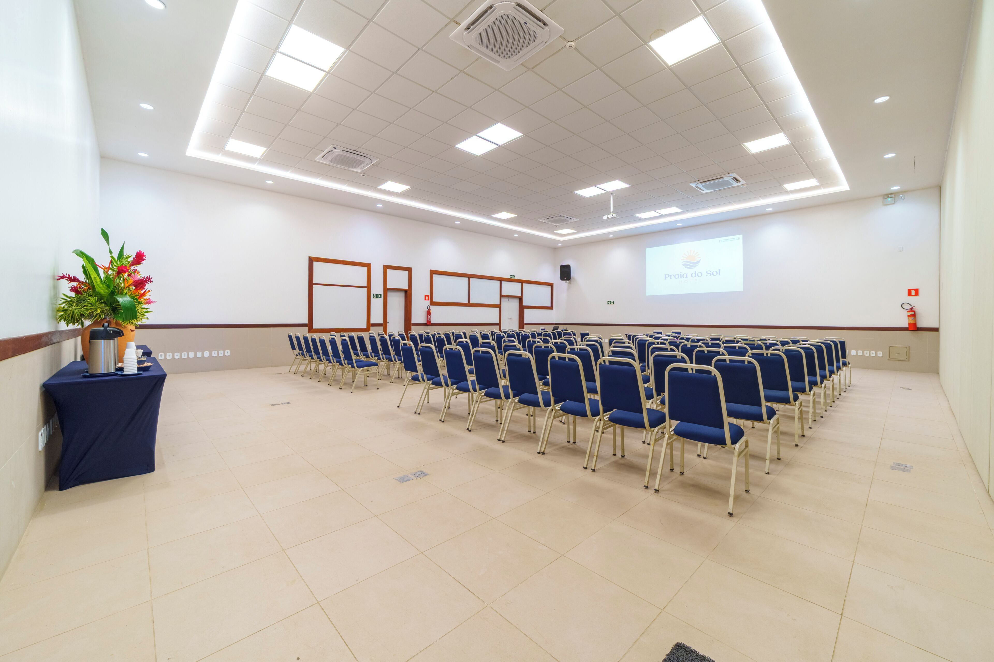 A conference room with rows of chairs, a projector screen, and a floral arrangement.