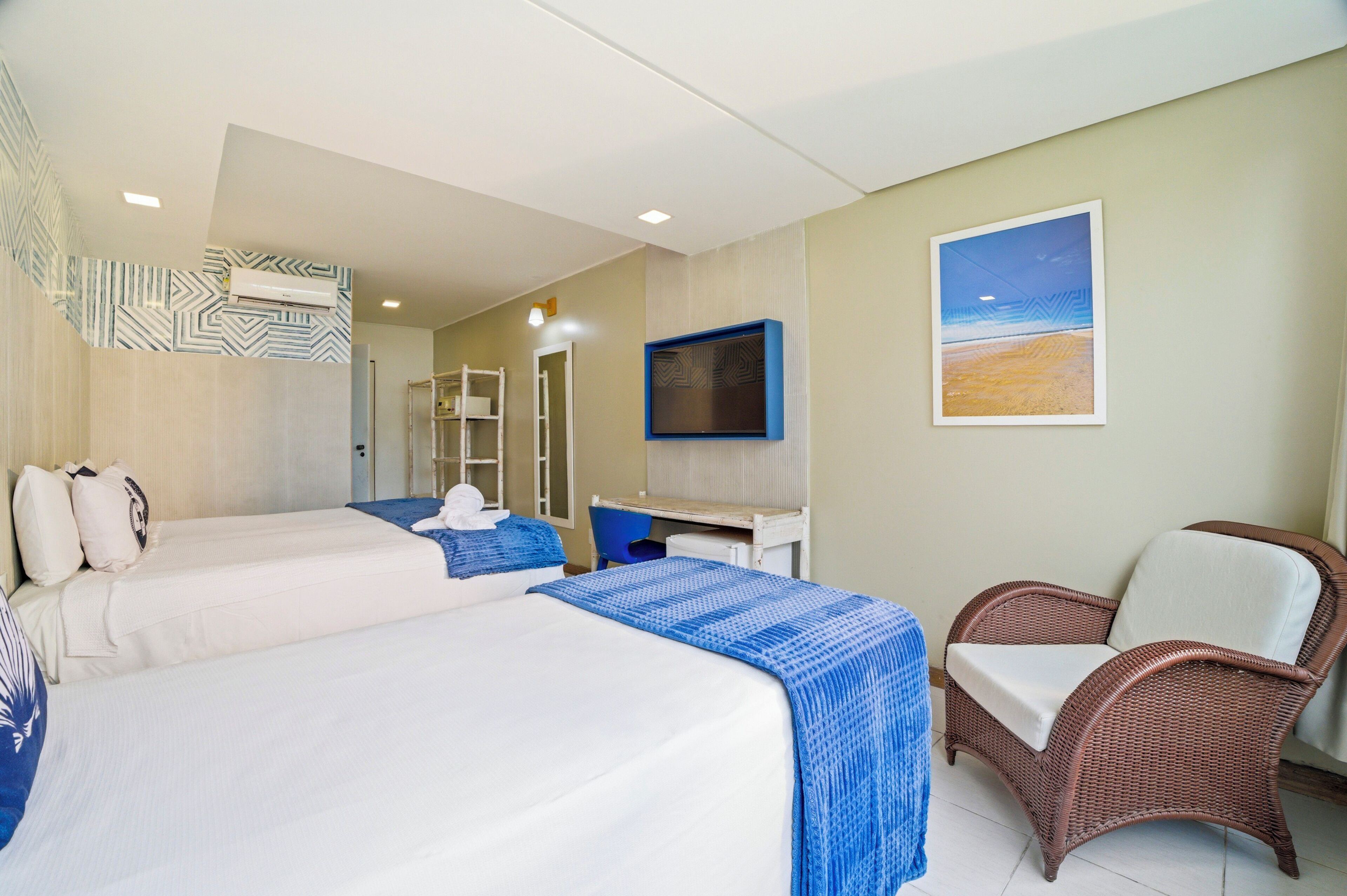 A hotel room with two beds, a desk, a chair, a TV, and a beach view.