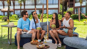 A group of people sitting on a blue patterned sofa outdoors with a table of food and drinks in front of them.