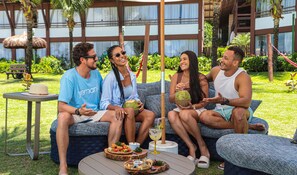 A group of people sitting on a blue patterned sofa outdoors with a table of food and drinks in front of them.