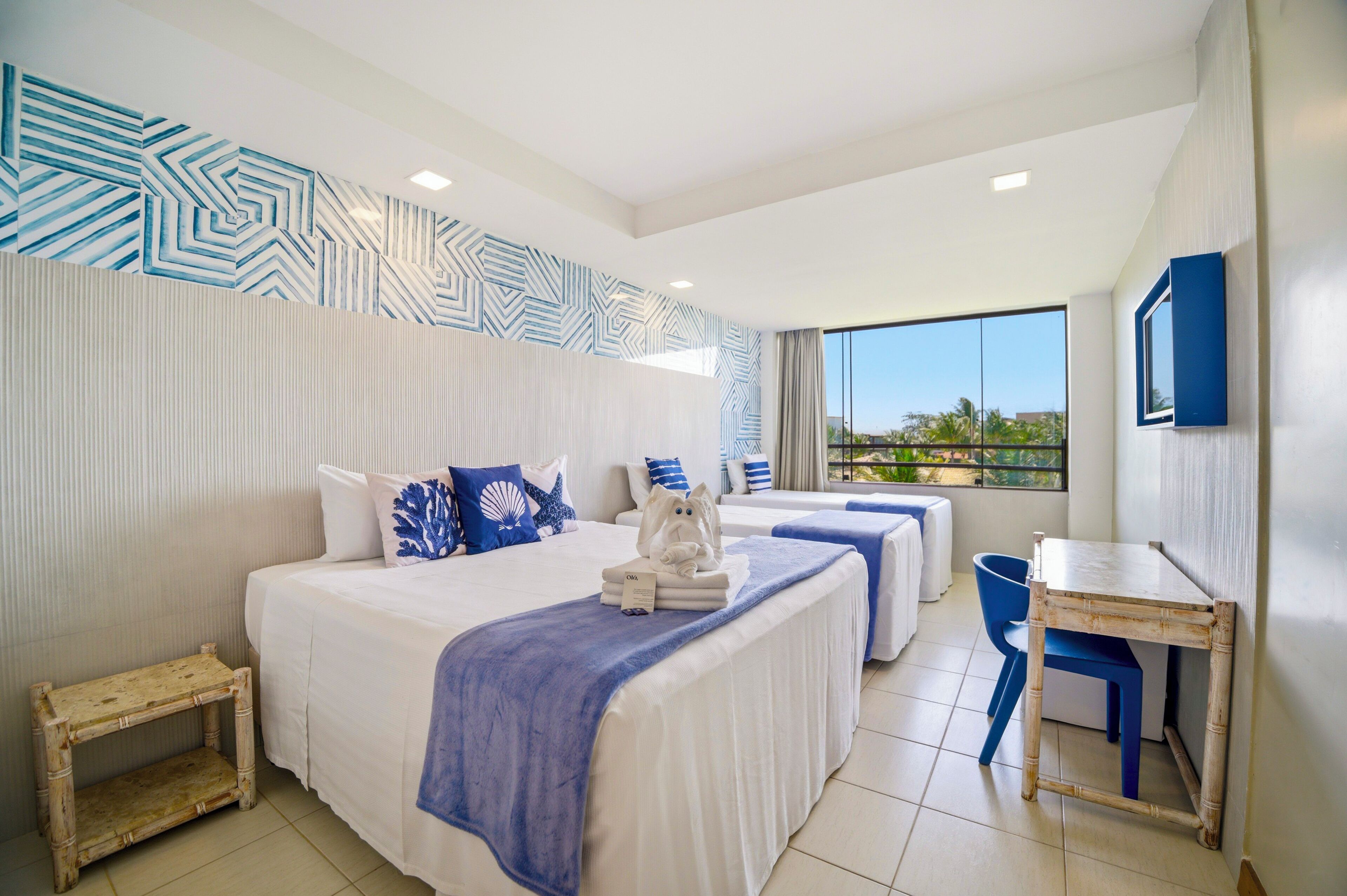 Habitación de hotel con dos camas, un escritorio y vistas al exterior.