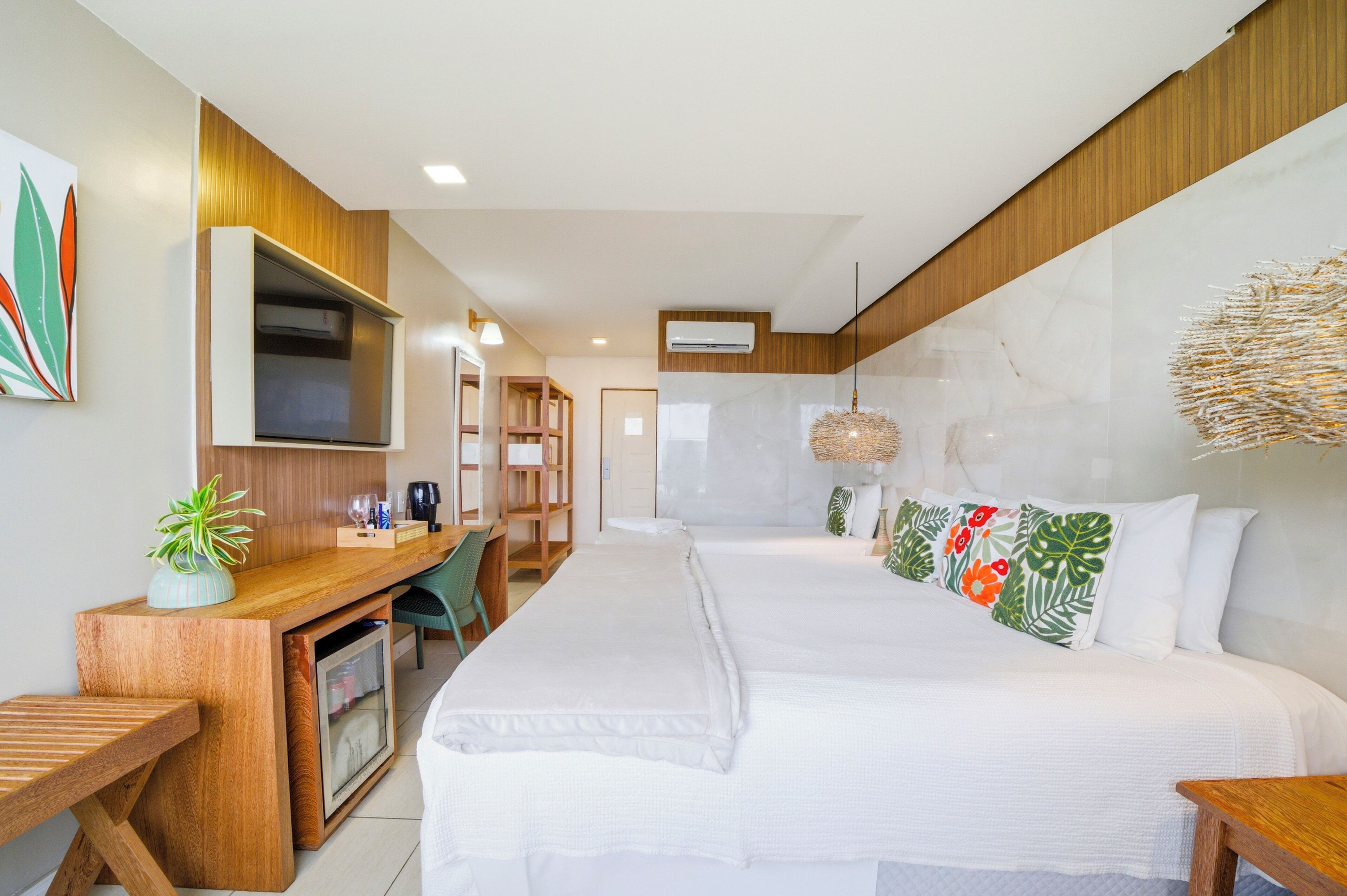Una habitación de hotel con cama, escritorio, silla, televisor y una planta.