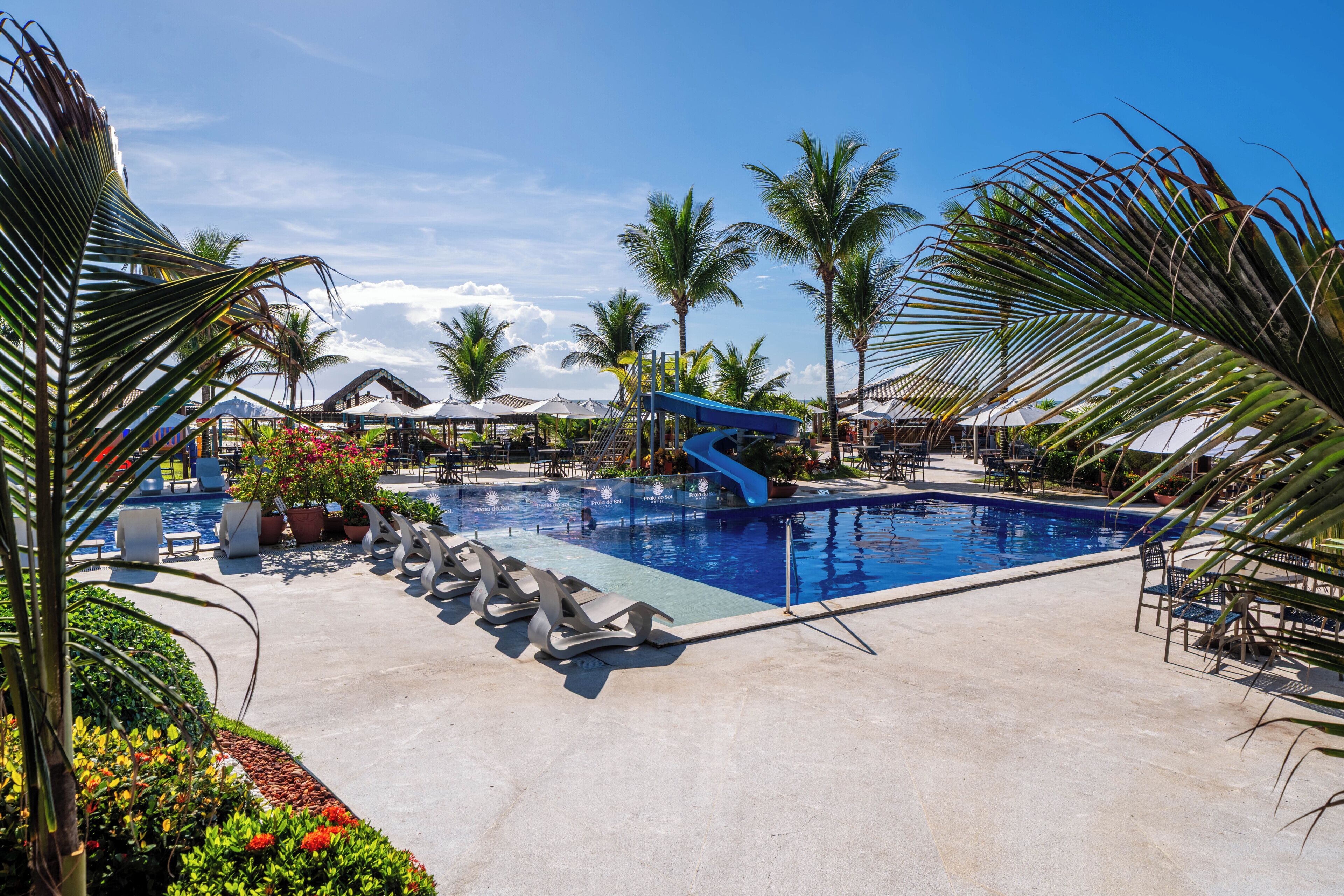 A resort pool area with a water slide, lounge chairs, and palm trees.