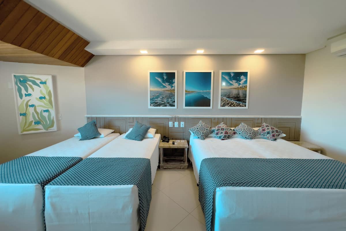 A hotel room with two beds, a nightstand, and a wall-mounted phone. There are three framed pictures above the beds.