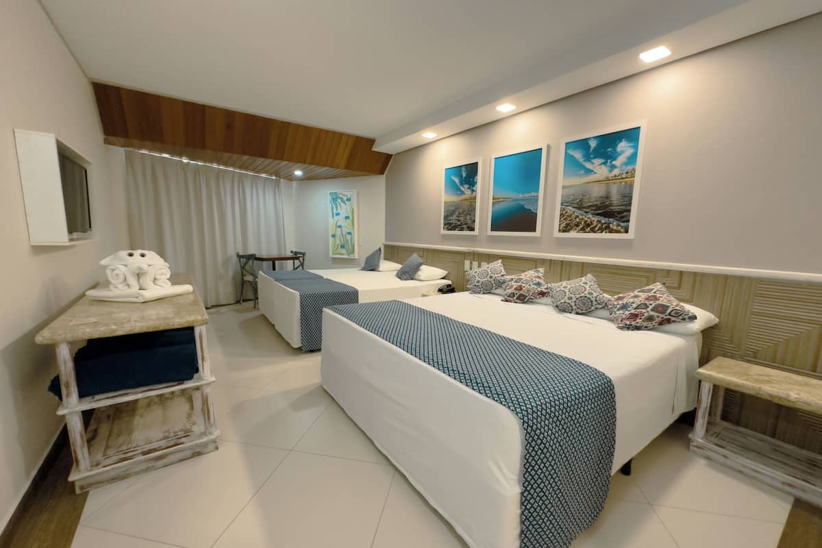 A hotel room with two beds, a desk, and a chair. There are three paintings on the wall.