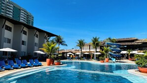 Una piscina con sillas de descanso y sombrillas, rodeada de edificios y palmeras.
