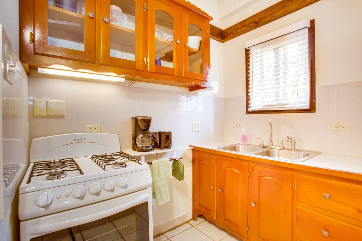 A kitchen with wooden cabinets, a stove, a sink, and a window with blinds.