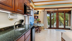 A kitchen with a granite countertop, stainless steel sink, and wooden cabinets. There is a water dispenser, a coffee maker, and a television on the wall. - Buttonwood Belize (Hopkins)