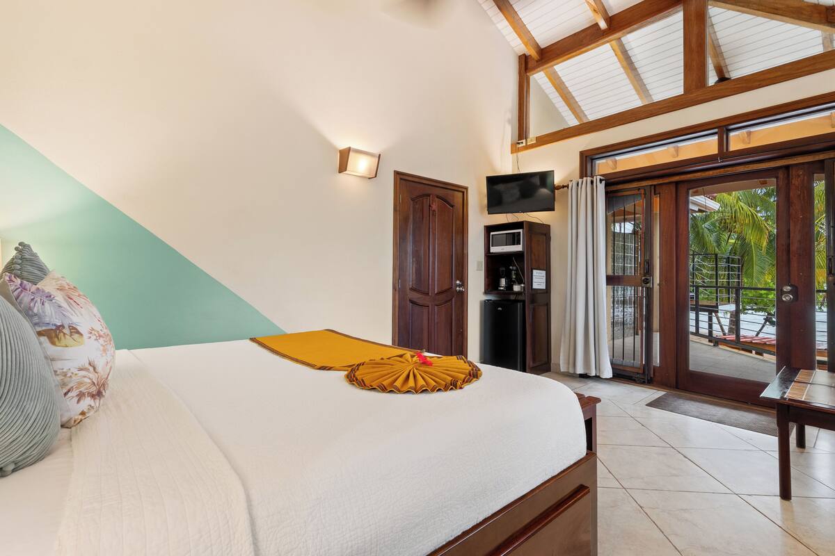 A hotel room with a bed, a television, a microwave, and a sliding glass door to a balcony.