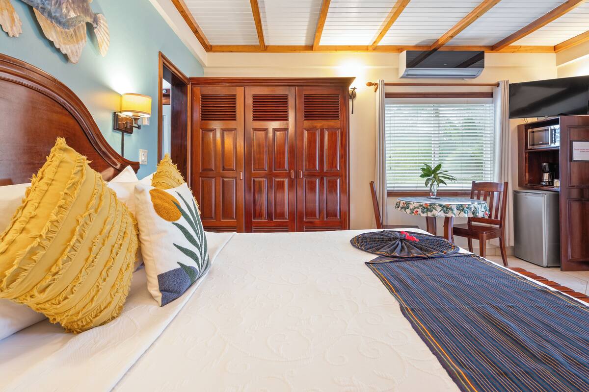 A hotel room with a large bed, wooden wardrobe, a small dining table, and a kitchenette.