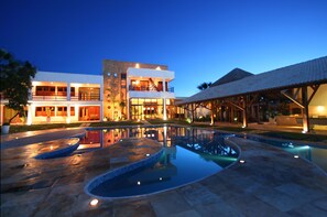 Un hotel moderno con zona de piscina, varias plantas e iluminación exterior.