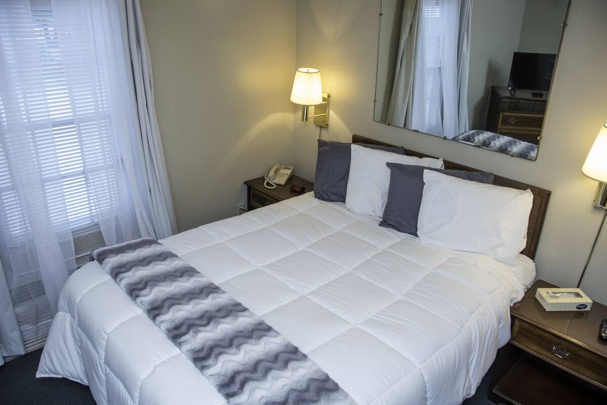 A hotel room with a large bed, a bedside table with a lamp, a phone, and a mirror.