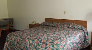 Una cama individual con colcha estampada, cabecera de madera, mesita de noche con teléfono y dos sillas.