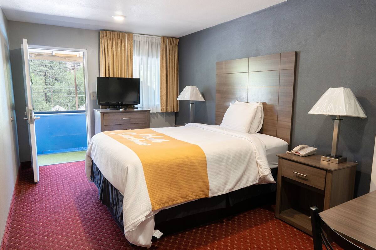 A hotel room with a bed, bedside lamps, a TV, a desk, and a view of the outside.