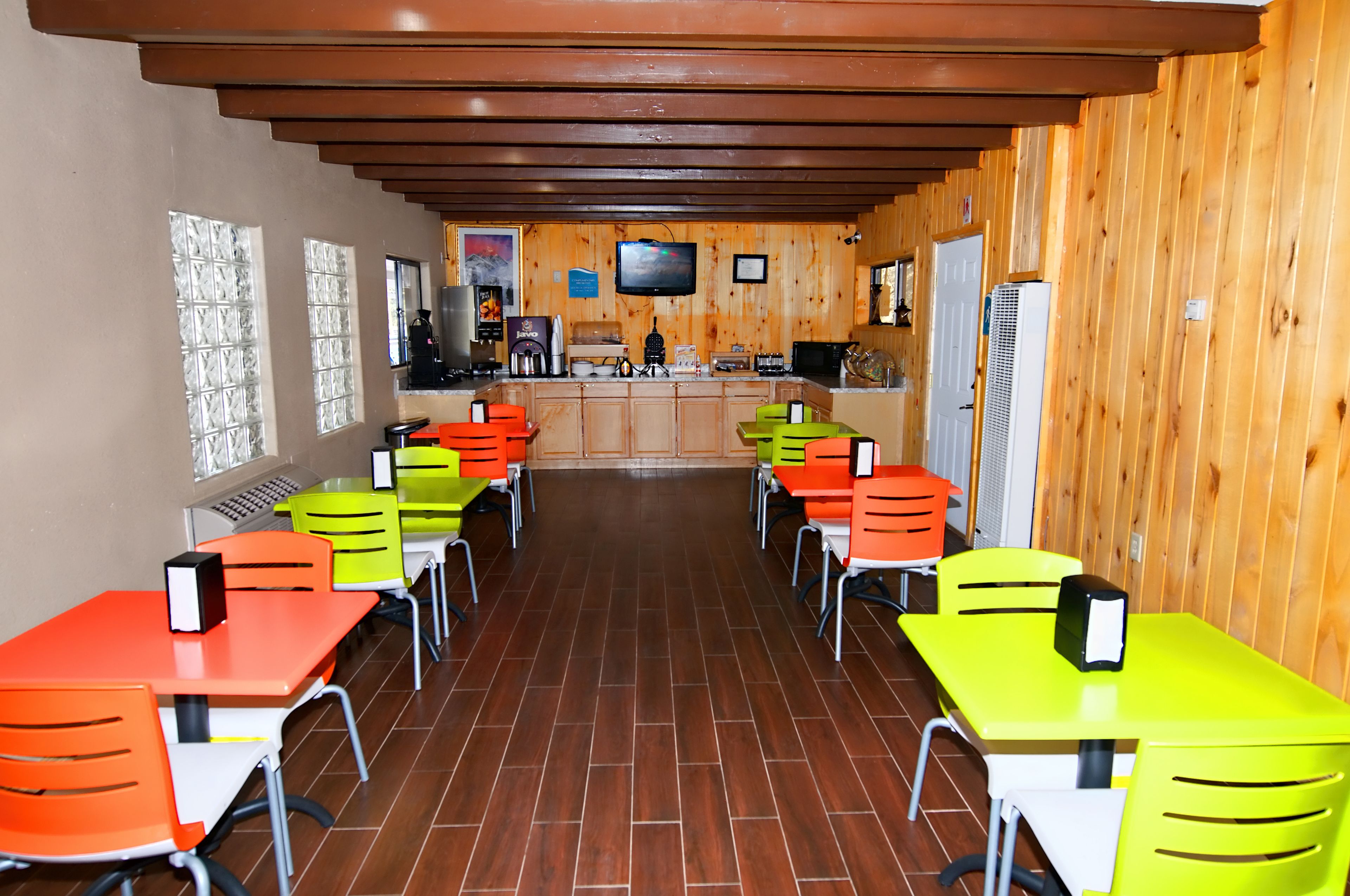 A restaurant with wooden walls, tiled flooring, and multiple tables and chairs in orange, green, and white.