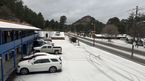 A parking lot with several cars and a building with blue columns. - Budget Lodge Ruidoso (Ruidoso)