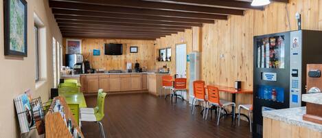 A wooden interior with a kitchen area, dining table, chairs, and a vending machine.