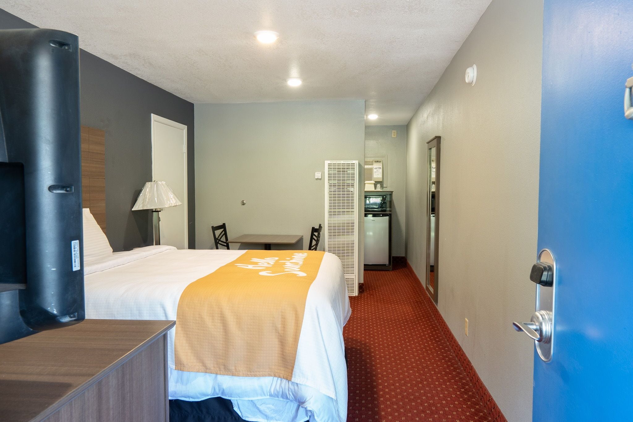 Une chambre d’hôtel avec un lit, un bureau, une lampe, un radiateur et une porte.