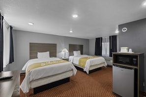 A hotel room with two beds, a minibar, a desk with a lamp, and a television.