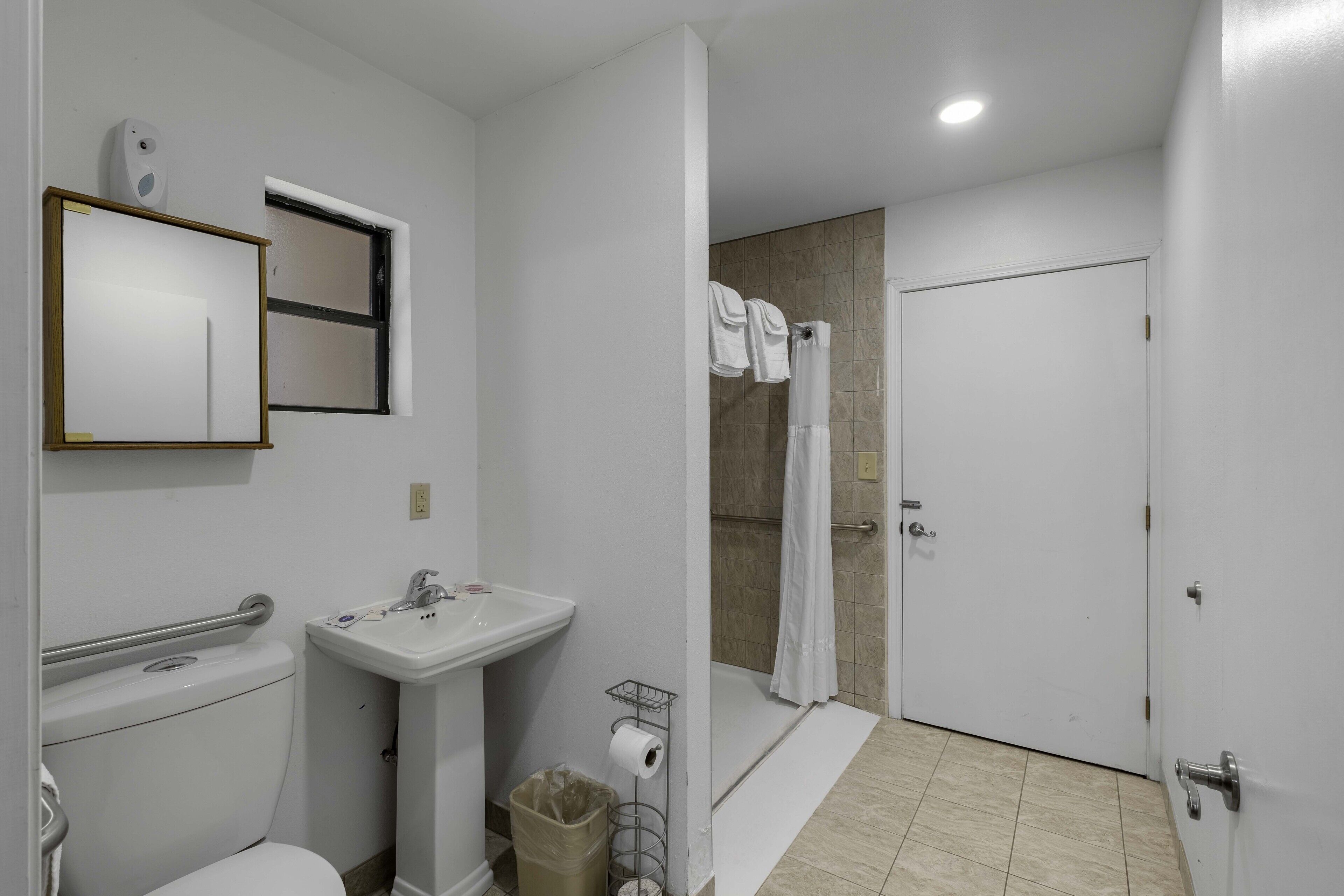 A bathroom with a toilet, sink, shower, and a door.