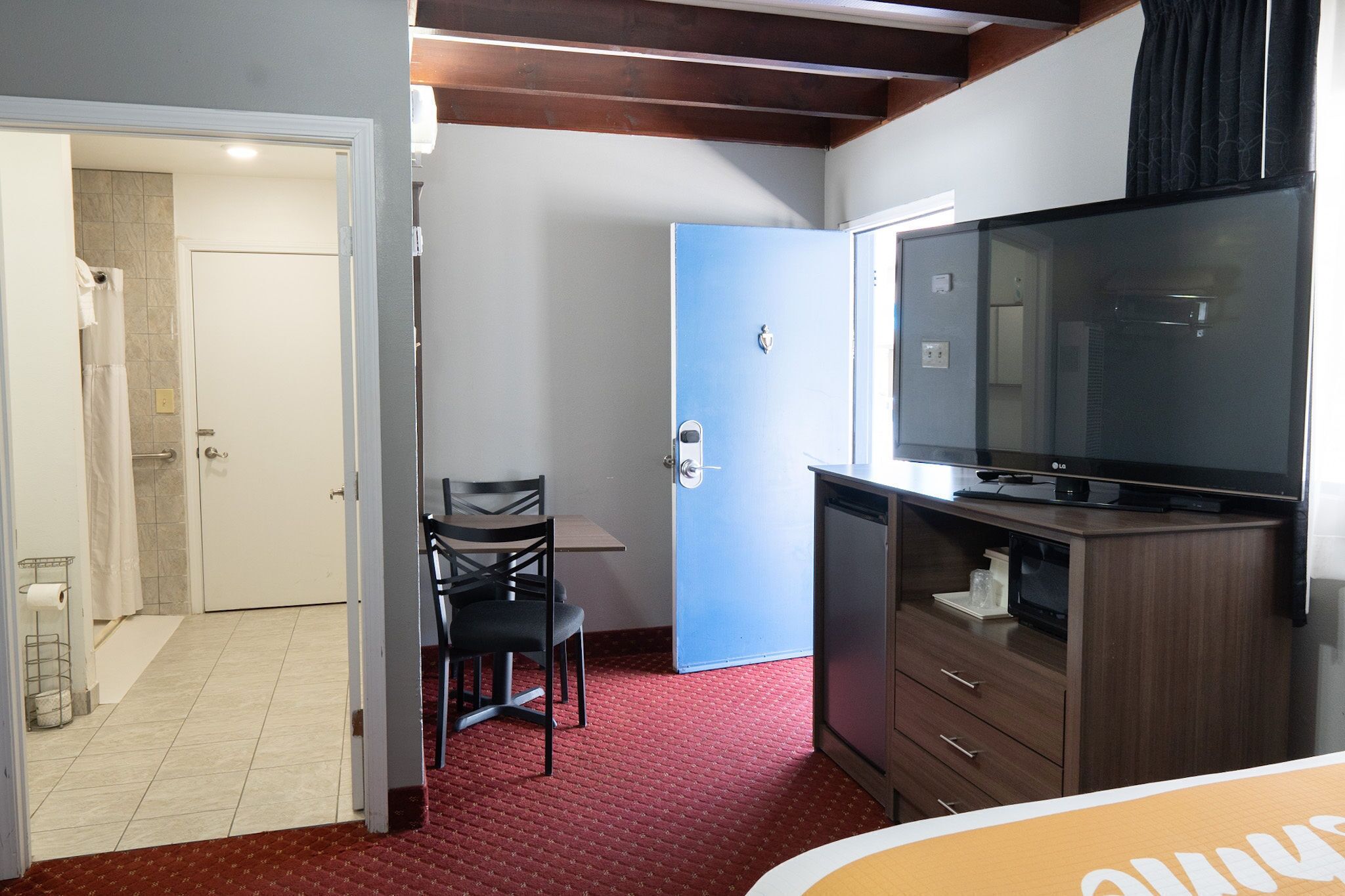 Habitación de hotel con televisión, escritorio y una silla. Se ve un baño con ducha y retrete a través de una puerta abierta.