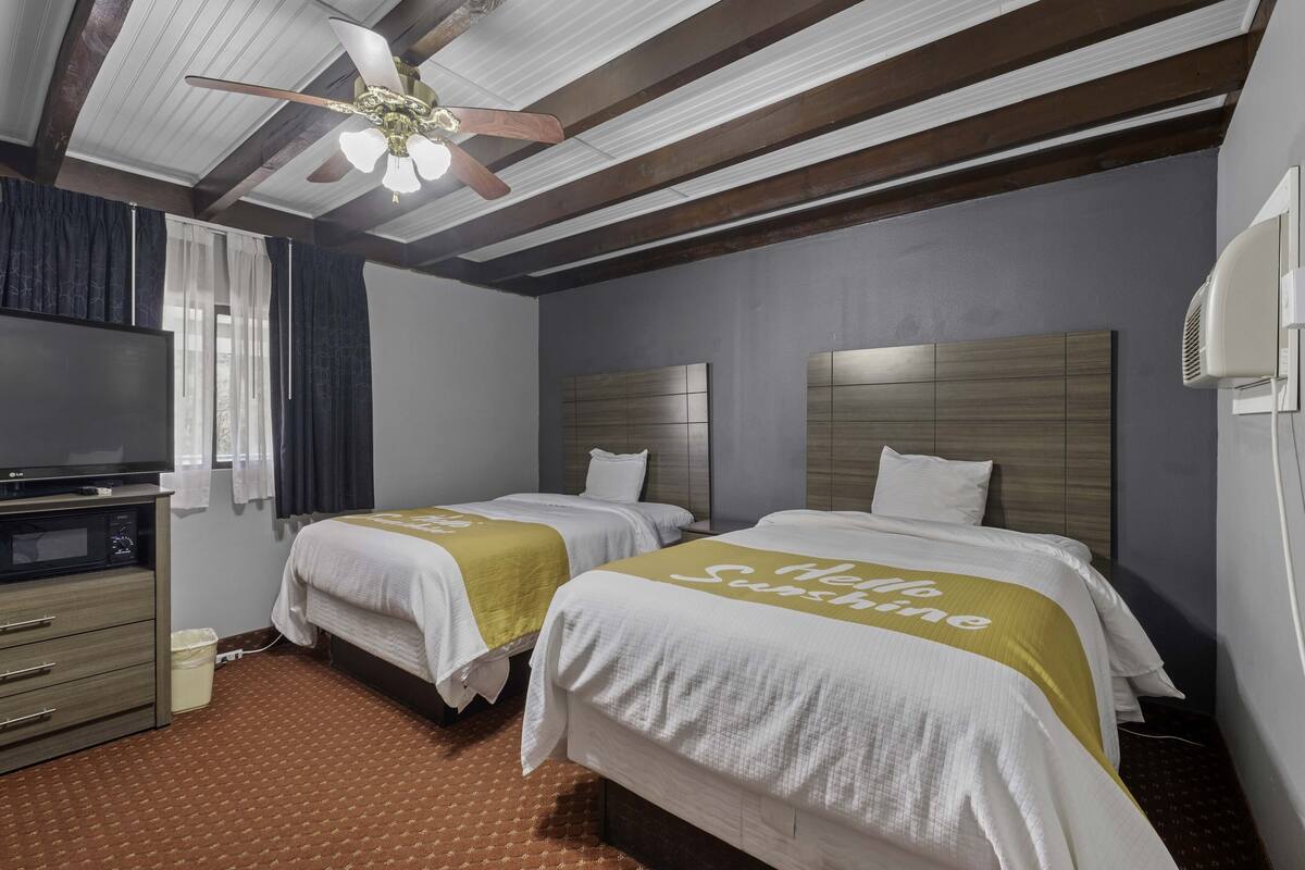 A hotel room with two beds, a TV, a ceiling fan, and a window with curtains.