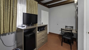 A compact room with a television on a wooden cabinet, a small refrigerator, a desk with a chair, and a white door. - Budget Lodge Ruidoso (Ruidoso)