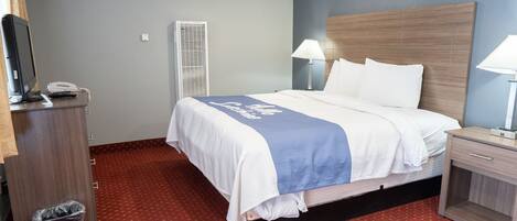 A hotel room with a bed, bedside lamps, a desk with a telephone, and a trash bin.