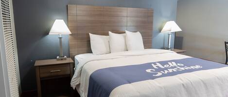 A hotel room with a bed, two bedside lamps, a nightstand, and a wall clock.